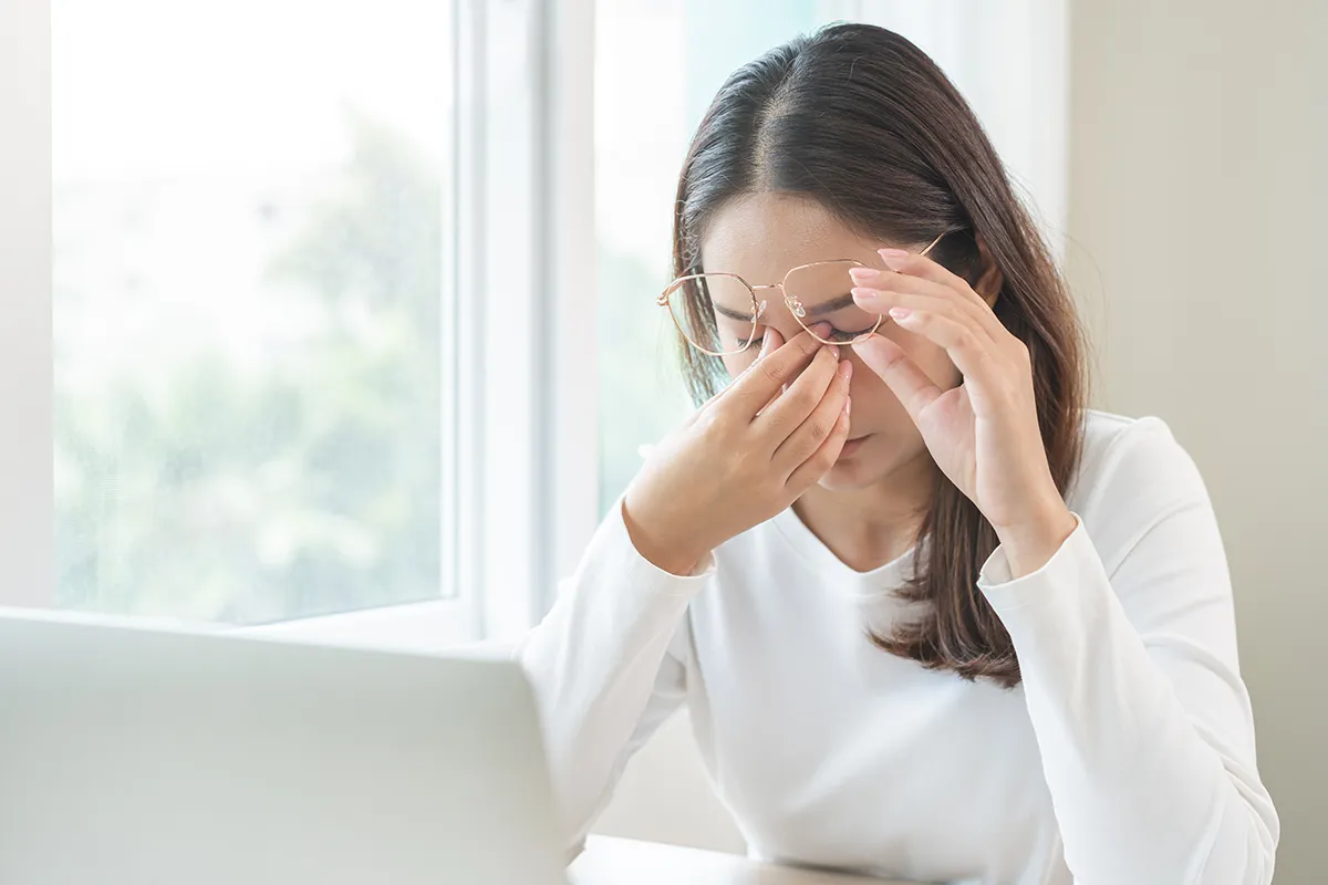 a woman at home working on her laptop and rubbing her tired, dry eyes