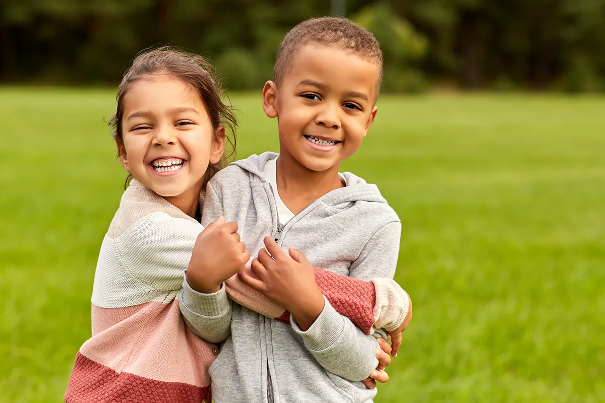 a little girl and boy smiling and hugging in the park