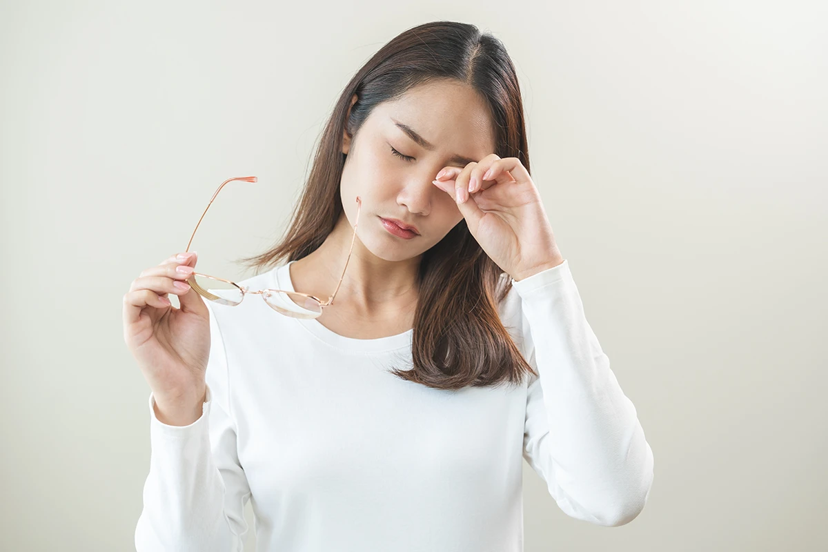 a young woman taking off her glasses and rubbing her eye