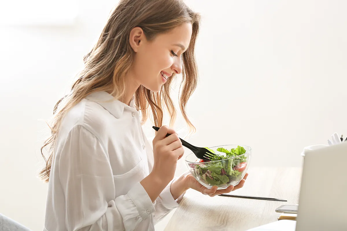 a smiling woman eating a salad in her office
