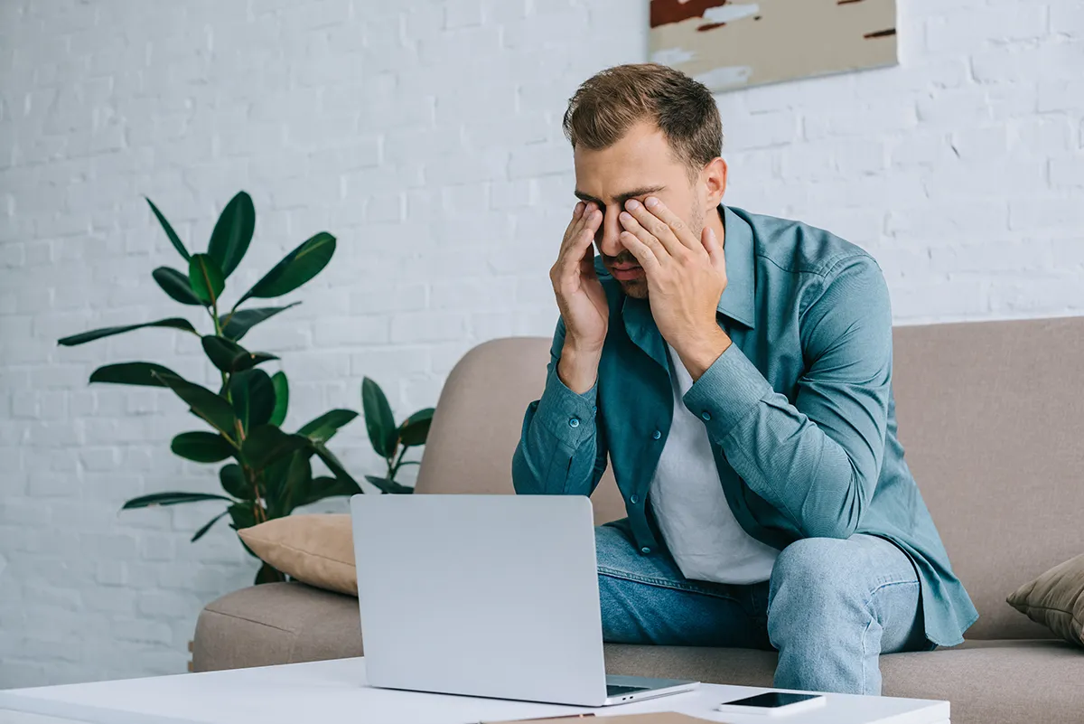 a young man rubbing his eyes while working at home