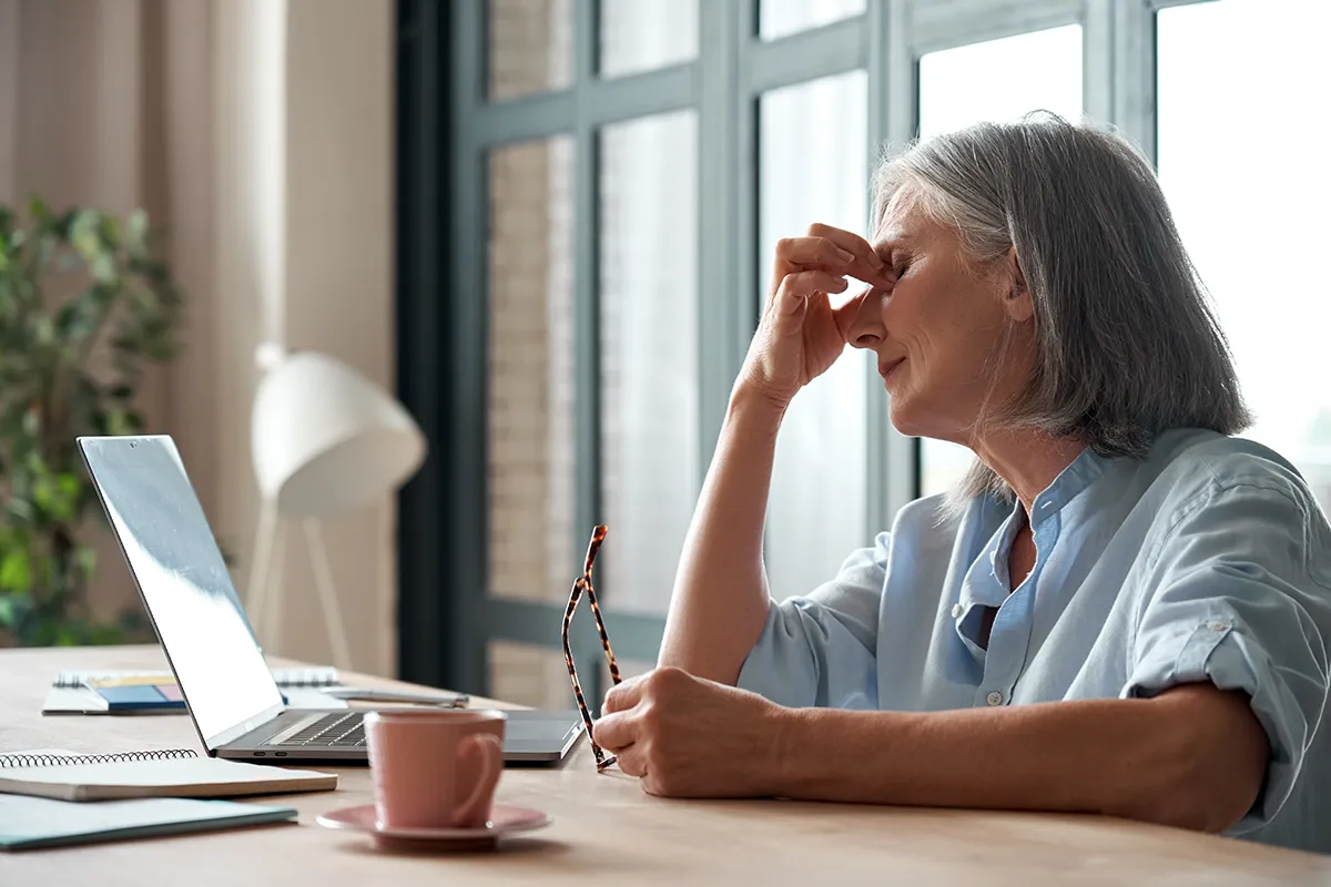 an older woman taking off her glasses and touching her face