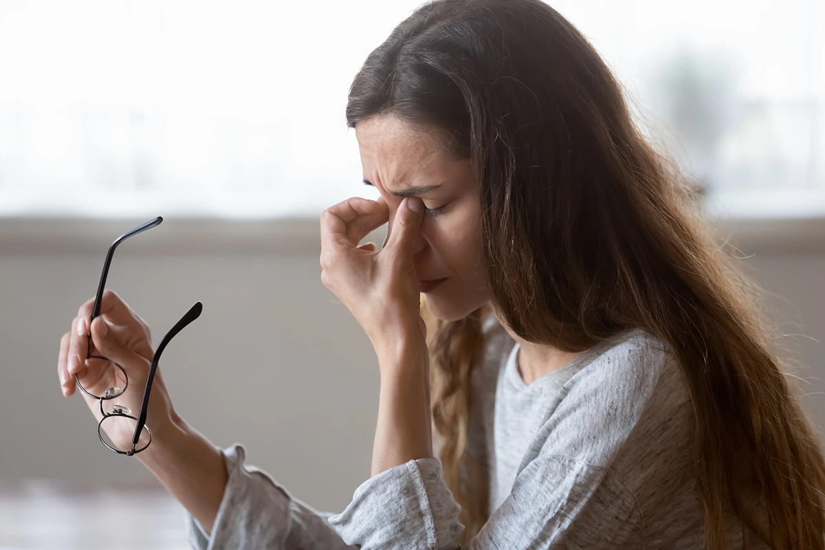 a woman taking off her glasses and massaging her eyes